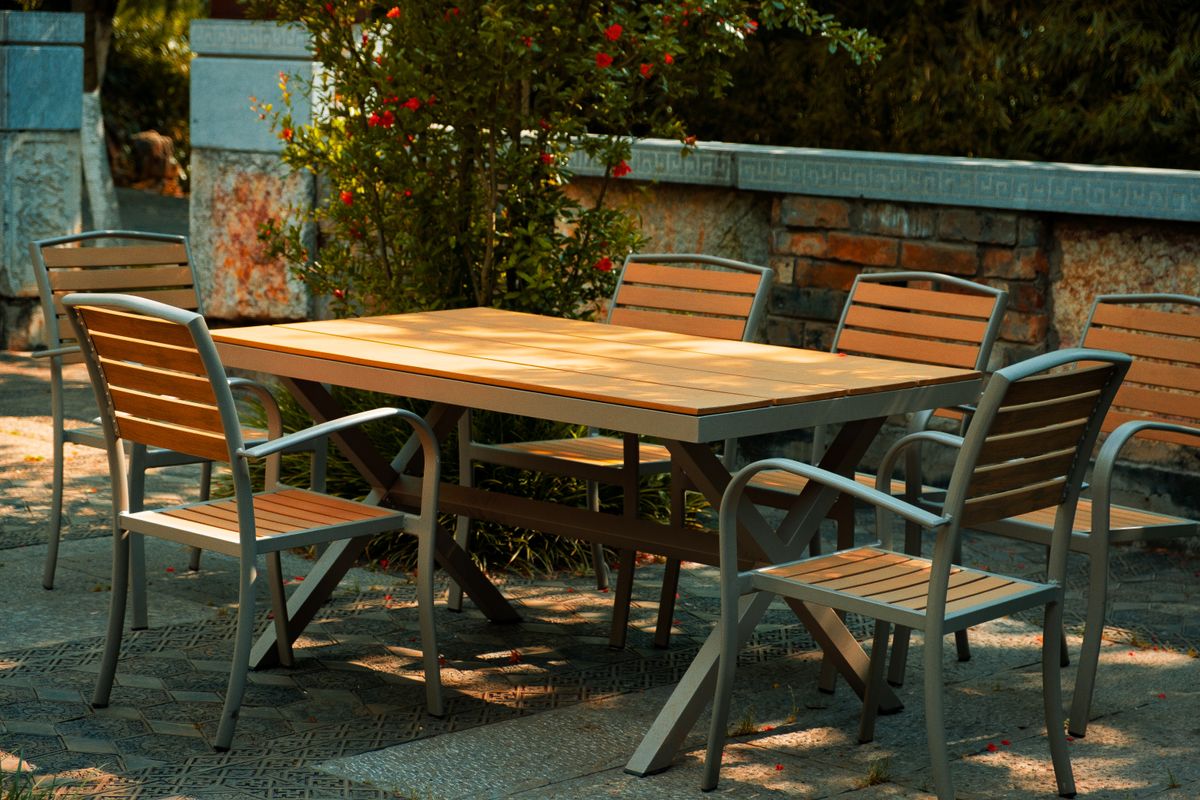 An outdoor dining table and empty wooden chairs surrounded by garden greenery